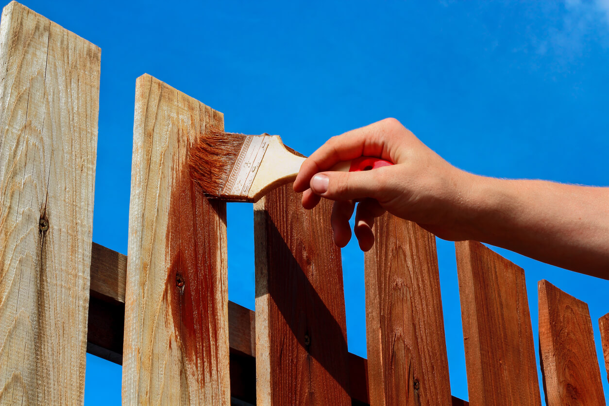 a person painting a fence a darker brown