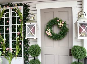 a green wreath with a few flowers in it on a front porch door